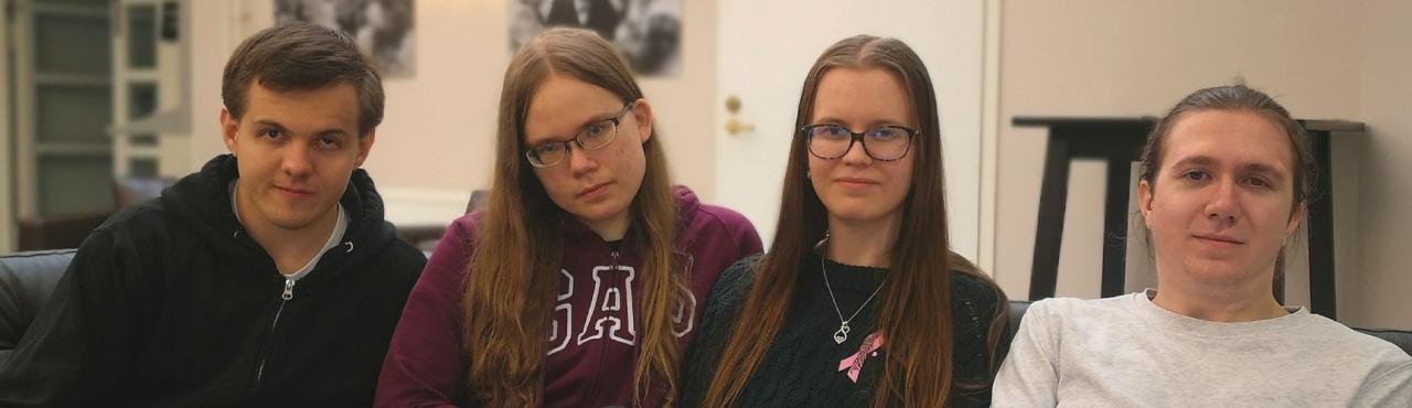 Neljä nuorta istuu sohvalla ja katsoo kameraan hymyillen.